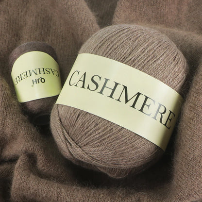 Two balls of brown cashmere yarn with visible labels on a textured fabric background.